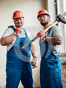 Two workers, holding a hammer and a sledgehammer in their hands