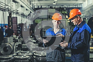 Two workers at an industrial plant with a tablet in hand, working together manufacturing activities