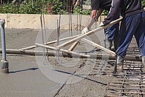 two workers leveling fresh concrete slab with a special wooden w