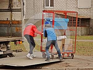 Two workers are loading a trolley with a cage for transporting goods onto the lift of a truck for transportation. Automation of