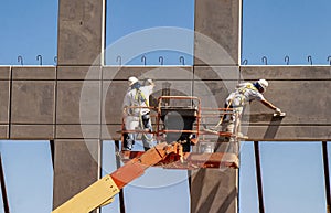 Two workers on man lift working on prefab wall using trowels