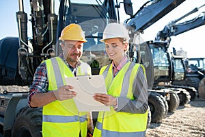 Two workers in open cast mine standing in front of heavy machinery