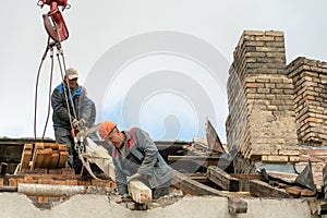 Two workers are repairing the roof of an old building. The carpenter holds a chainsaw in his hand. A wooden beam is attached to