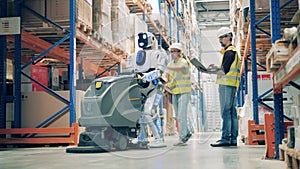 Two workers restart stopped warehouse robot with vacuum cleaner