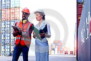 Two workers with safety helmet at logistic shipping cargo containers yard. African American engineer man using digital tablet and