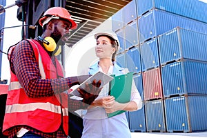 Two workers with safety helmet at logistic shipping cargo containers yard. African engineer man using digital tablet to report