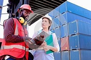 Two workers with safety helmet at logistic shipping cargo containers yard. African engineer man using digital tablet to report