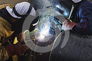 Two workers together welding big tube