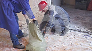 Two workers in uniform carries bags of construction debris from the building