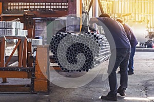 Two workers in uniform using lifting machines to move metal pipe in a sheet metal factory