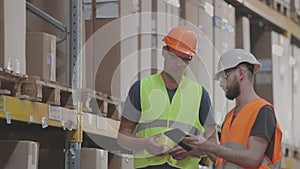 Two workers in a warehouse are discussing work. Engineers in a factory warehouse