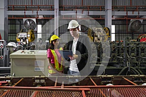 Two workers, wearing hard hats, stand side by side near large machinery at a construction site