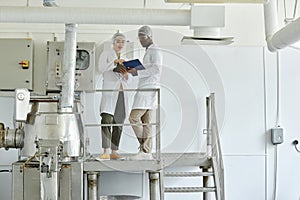 Two workers wearing lab coats in factory workshop