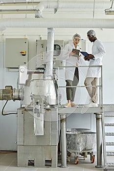 Of two workers wearing lab coats using laptop in clean factory workshop