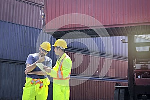 Two workers wearing safety clothing and helmet standing and  discussing something with forklift truck handling container box at