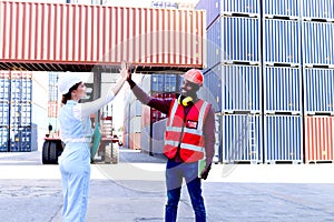 Two workers wearing safety helmet making high five hand touch at logistic shipping cargo containers yard. African male engineer