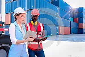 Two workers wearing safety vest and helmet discussing at logistic shipping cargo container yard. African American engineer man