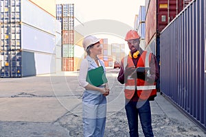 Two workers wearing safety vest and helmet discussing at logistic shipping cargo containers yard. African American engineer man