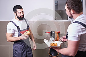 Two workers wearing uniform eating burger during lunch break