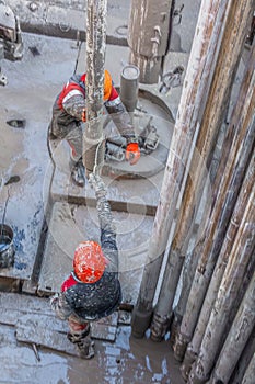 Two working drillers install a drill pipe raised from the well.