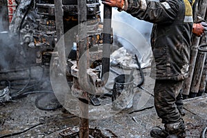 Two working drillers in a uniform, in a helmet and goggles, install drill pipes after lifting them from an oil well