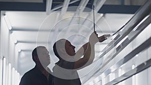 Two working male painters prepare steel metal elements for painting by fixing them on suspensions. Paint parts in the