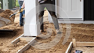 Two working men shovel dirtfor a new cement concrete sidewalk.