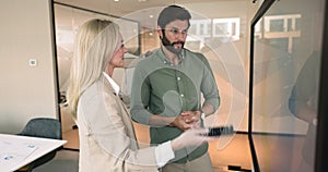 Two workmates stand at TV screen discussing shown visual data