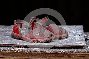 Two worn-out red sandals with buckles, lying on a dusty and dirty surface