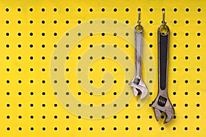 Two wrenches hang from hooks on yellow pegboard