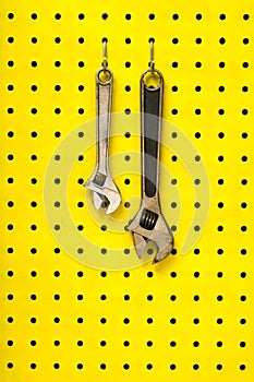 Two wrenches hang from hooks on yellow pegboard