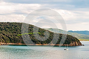 Two yahts floating near the scenic landscape of Cala Violina beach in Tyrrhenian Sea bay surrounded by green forest in province of