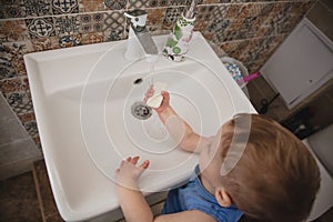 Two-year-old blond baby washes his hands at home over the sink