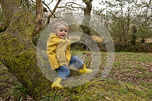 Two year old boy in yellow raincoat and welly boots playing