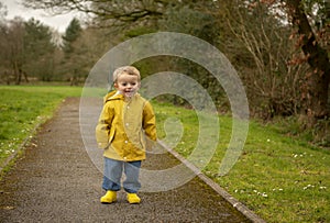 Two year old boy in yellow raincoat and welly boots playing outdoors