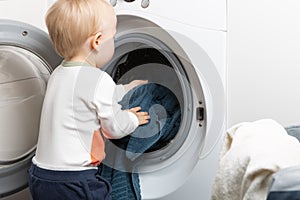 Two year old child doing household chores. Loading washing machine