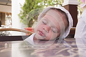 Two-year-old girl asleep at a table in the street cafe