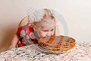 A two-year-old girl bites pancakes. Maslenitsa festival