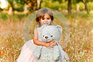 Two-year-old girl in field carrying stuffed animal