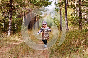 Two-year-old girl in golden vest walks in the forest in autumn