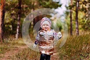 Two-year-old girl in golden vest walks in the forest in autumn