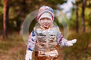 Two-year-old girl in golden vest walks in the forest in autumn