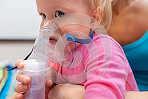 Two year old girl making inhalation with nebulizer at home with mother. The treatment of child with inhaler and