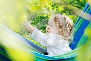 Two year-old toddler girl is laughing and playing in striped blue-green Brazilian hammock