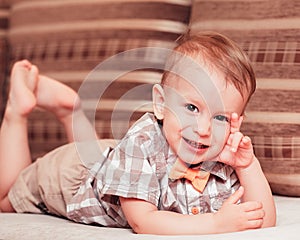 Two years old baby boy in t-shirt and a bow-tie lying on his stomach and smiling