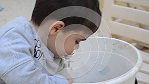 Two years old boy playing with dirt from the white bucket