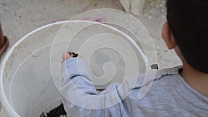 Two years old boy playing with dirt from the white bucket