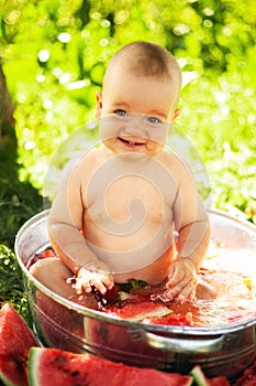 Two years old child eating piece of watermelon on the grass in garden. Dirty face, happy and emotional kid, juicy watermelon.