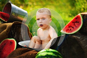 Two years old child eating piece of watermelon on the grass in garden. Dirty face, happy and emotional kid, juicy watermelon.