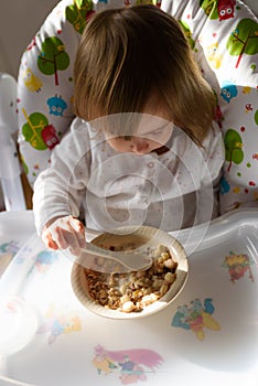 Two years old eats brakefast by herself with a spoon